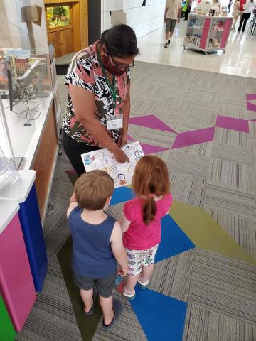 Rosie shows two children the Summer Reading Challenge game board