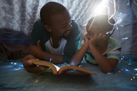 Man and child reading together in a blanket fort